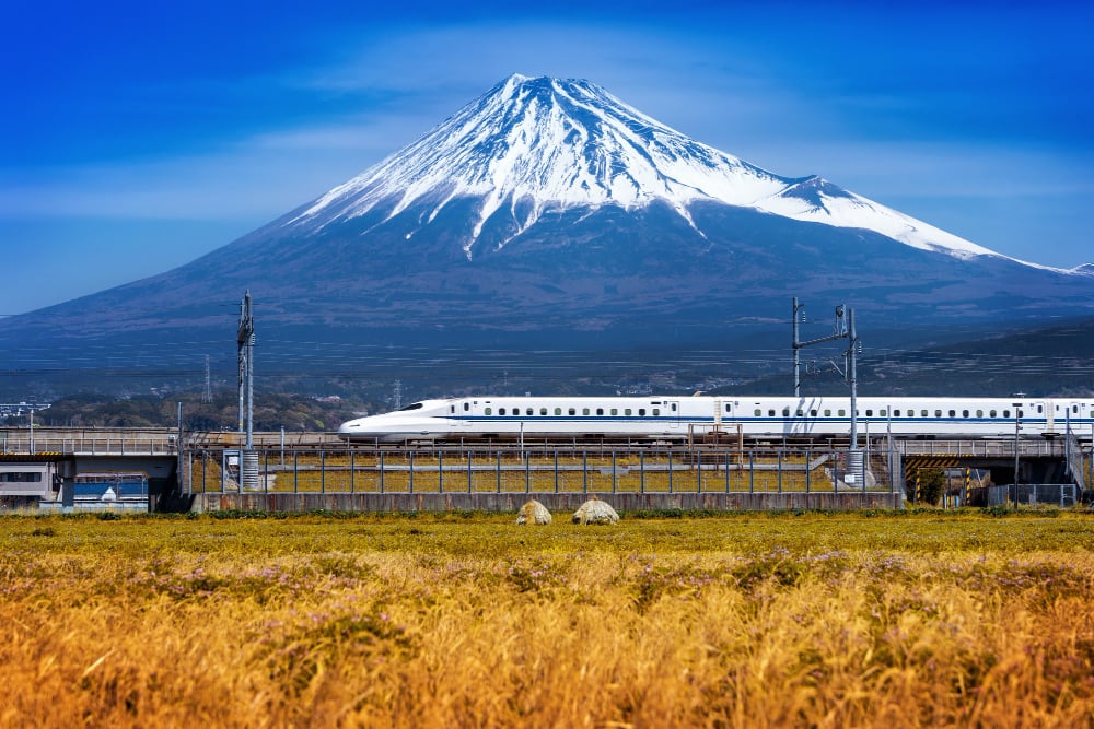 Shinkansen bullet train passing in front of snow-capped Mount Fuji in Japan