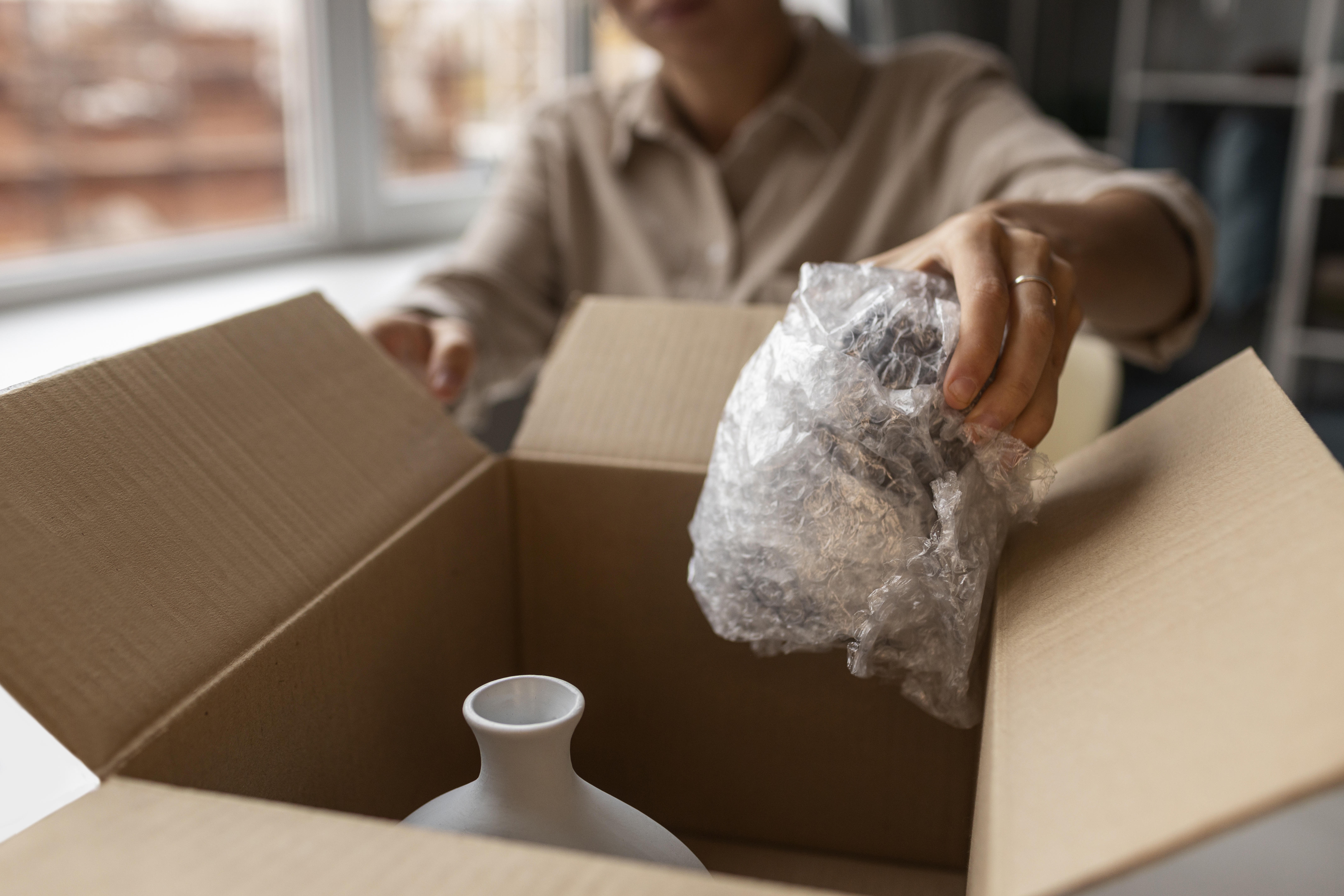 Packing fragile objects at home—protective wrap cushioning a delicate vase inside a box.