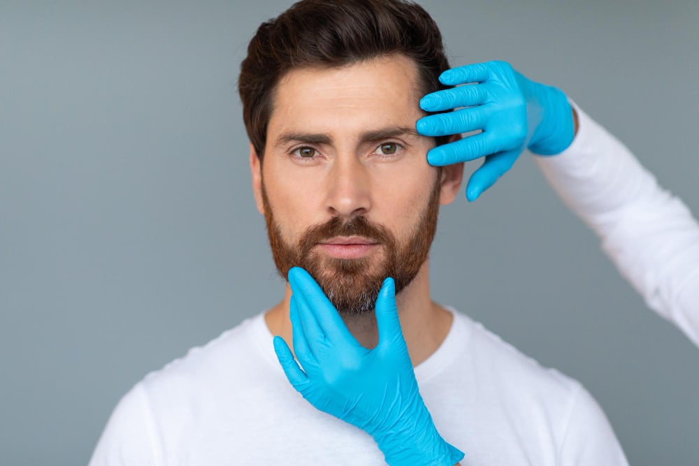 Photo plastic surgery and aesthetic cosmetology concept cosmetician hands in protective medical gloves touching male face
