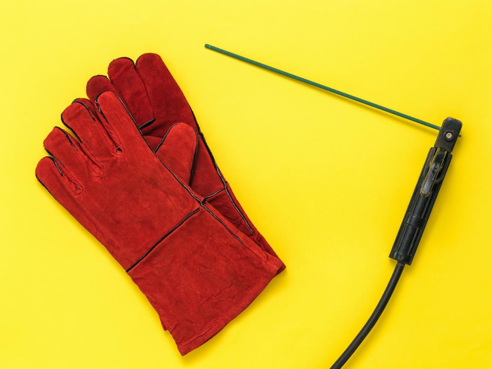 Photo red welder's gloves and a handle with an electrode on a yellow background protective accessory for welding operations
