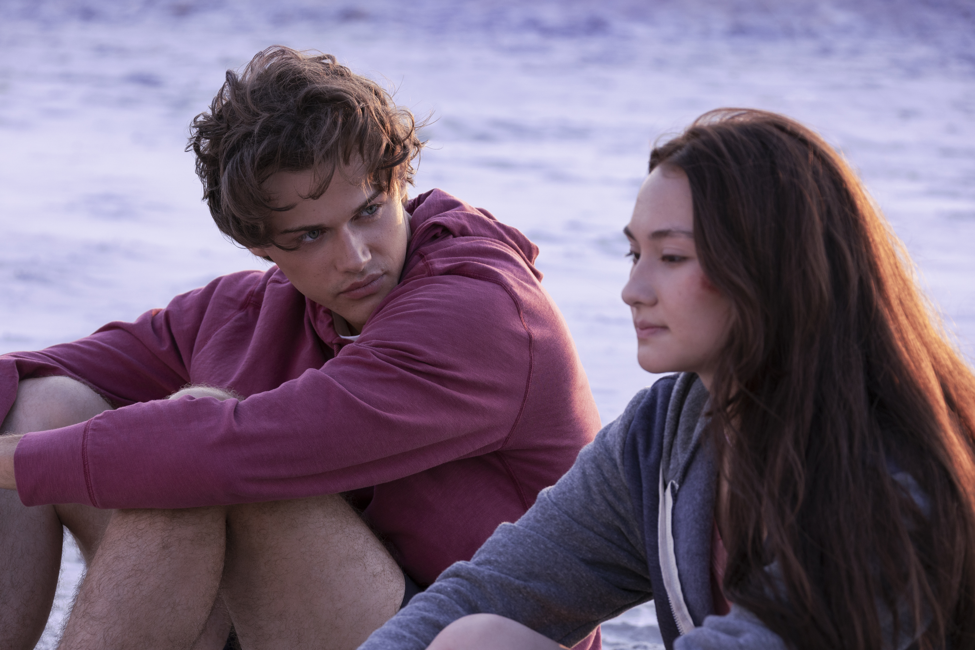 Christopher Briney as Conrad and Lola Tung as Belly sitting on the beach in The Summer I Turned Pretty