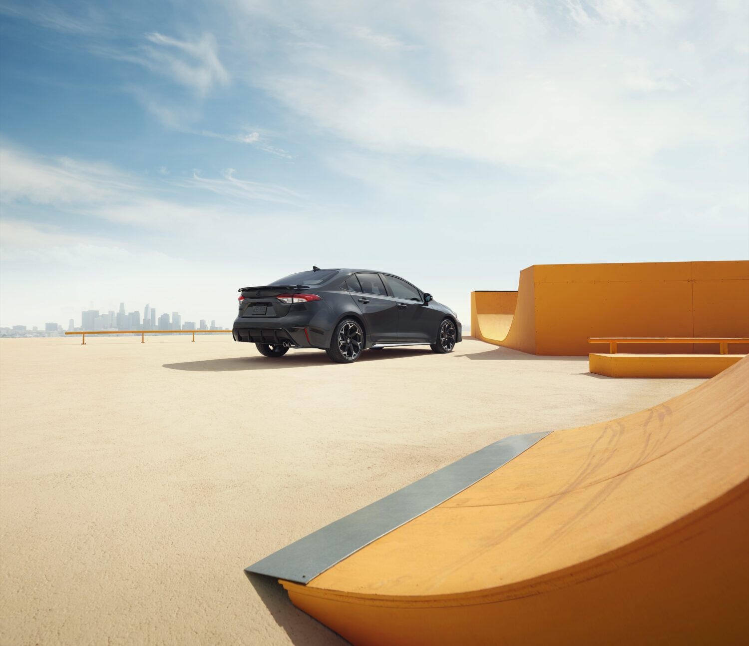 Rear view of the 2025 Toyota Corolla FX in black parked near a skate-style backdrop