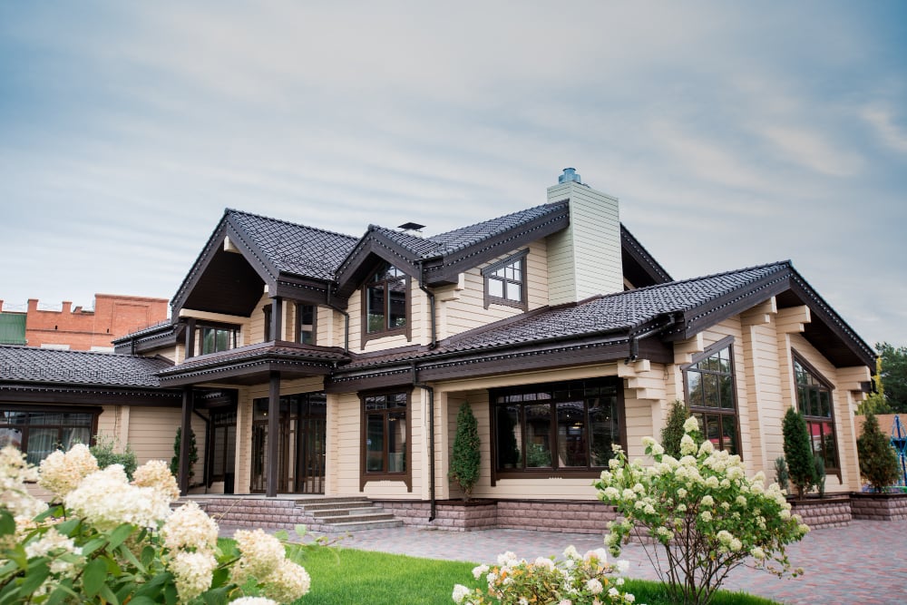 Photo view of luxurious modern house with decorative elements around windows and front yard with blooming white flowers