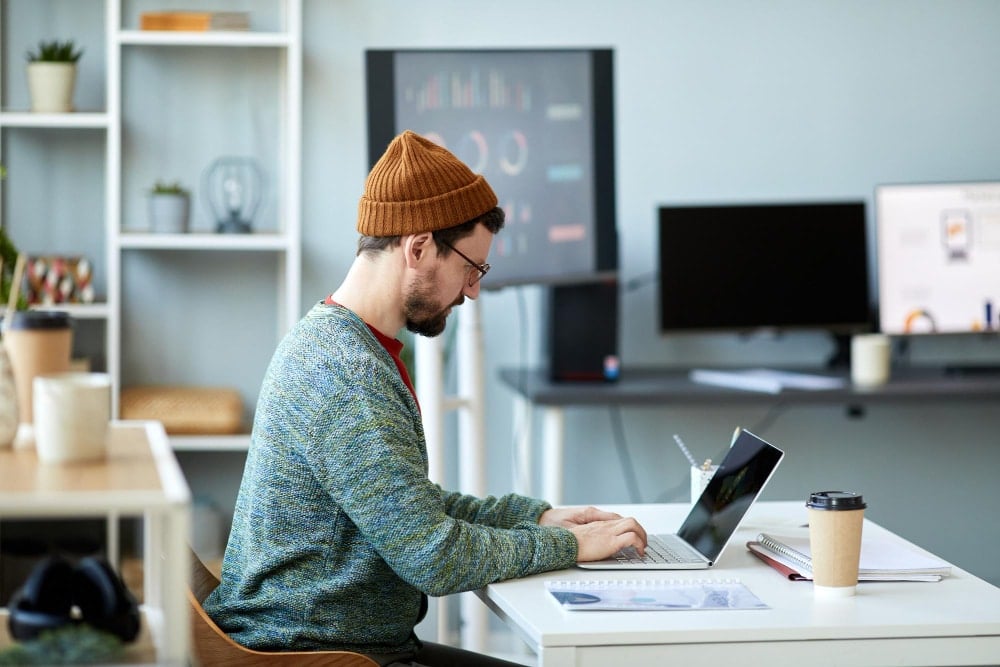 Young male employee or designer sitting by desk in front of laptop in office and analyzing online da