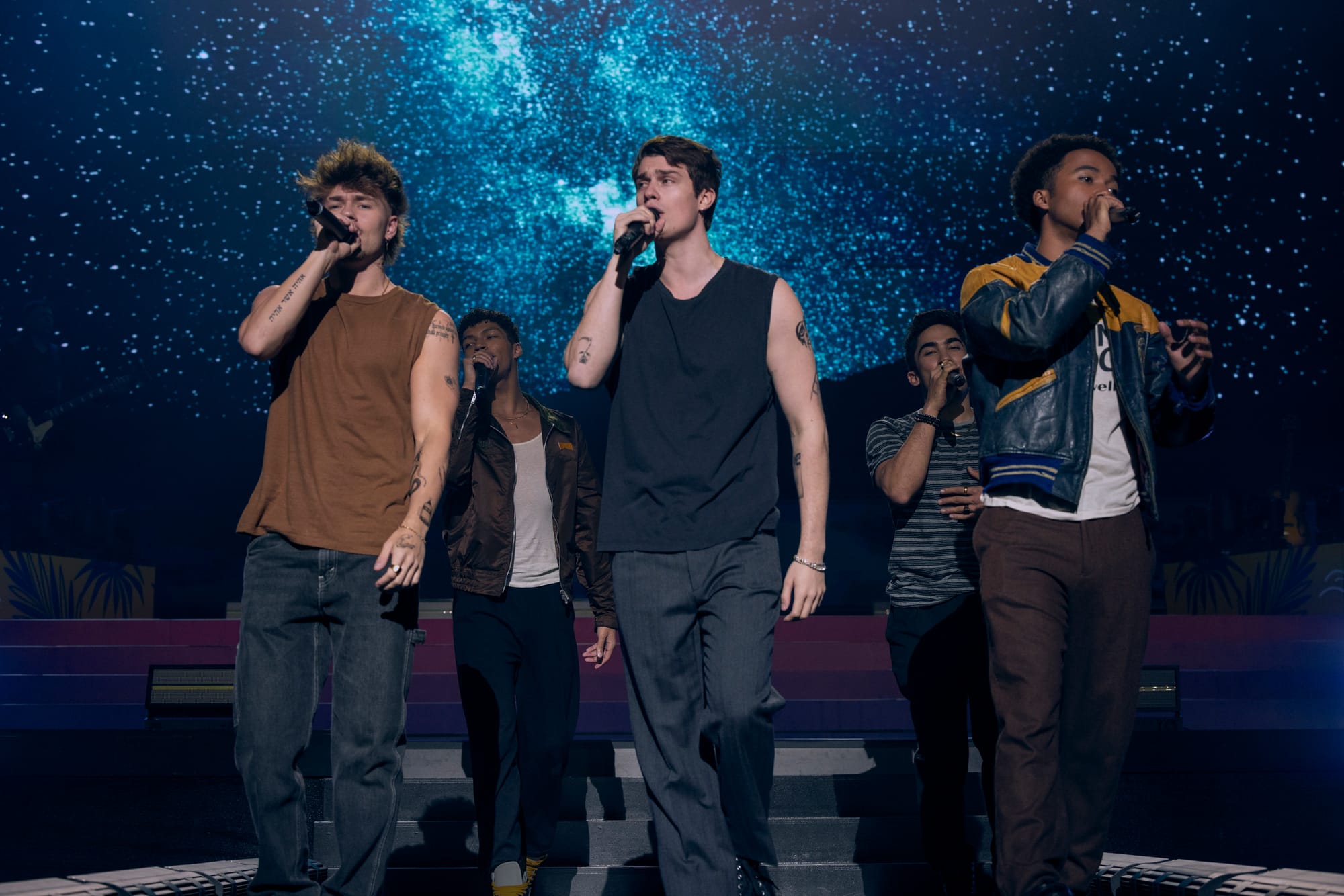 A popular boy band performs on stage under dramatic lighting during a concert scene in The Idea of You.