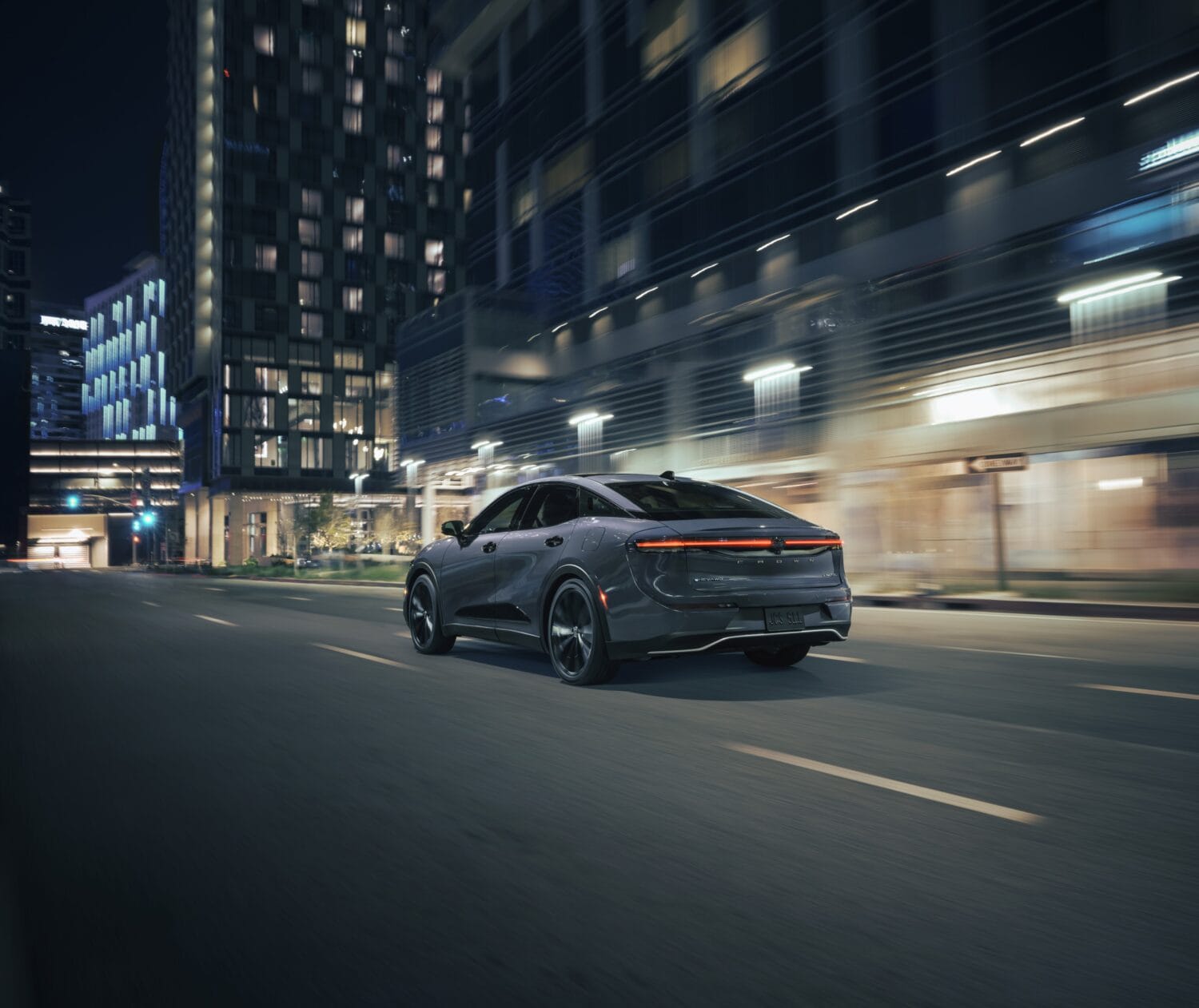 Rear view of the 2026 Toyota Crown Nightshade driving through a modern city at night with full-width LED taillight