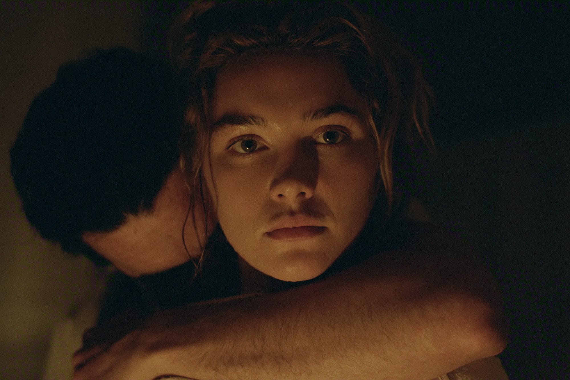 Close-up of a woman looking past a man’s shoulder as they embrace in a dimly lit East of Eden scene.