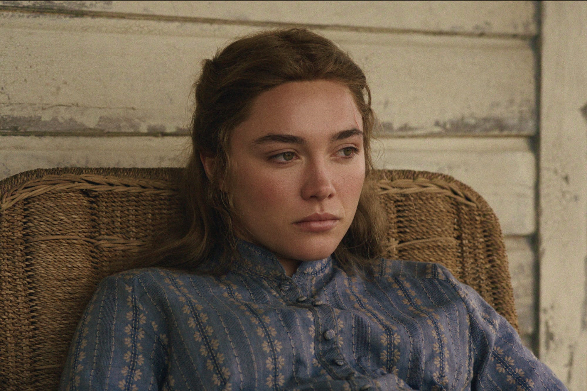 A woman wearing a blue patterned dress sits in a wicker chair in East of Eden.