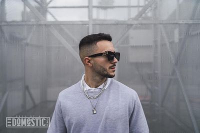 Stylish young attractive man wearing a sweater over a shirt with necklaces and sunglasses