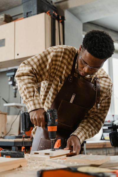A focused carpenter using a drill in a woodworking workshop, showcasing craftsmanship.