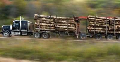 A logging truck transports timber swiftly along a rural highway.