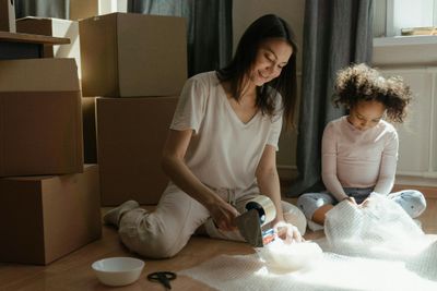 A mother and daughter packing boxes while preparing for a move in a sunlit room.
