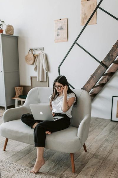 A woman sits comfortably on a sofa using a laptop in a modern living room.