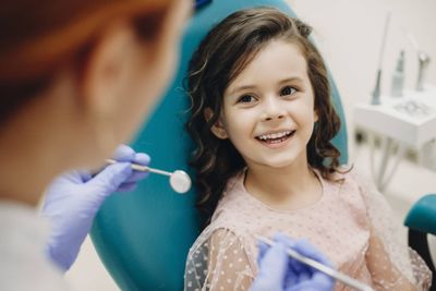 Lovely little kid smiling while talking with the pediatric dentist after doing a tenth examination in a pediatric stomatology