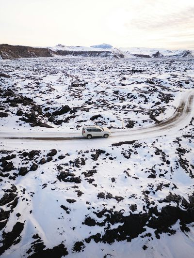 Aerial view of an SUV navigating a snowy Icelandic landscape, capturing winter's serene isolation.