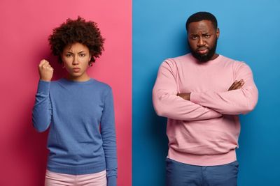 Angry dissatisfied woman clenches fist and shows her power, black unshaven man stands near with arms folded, express negative