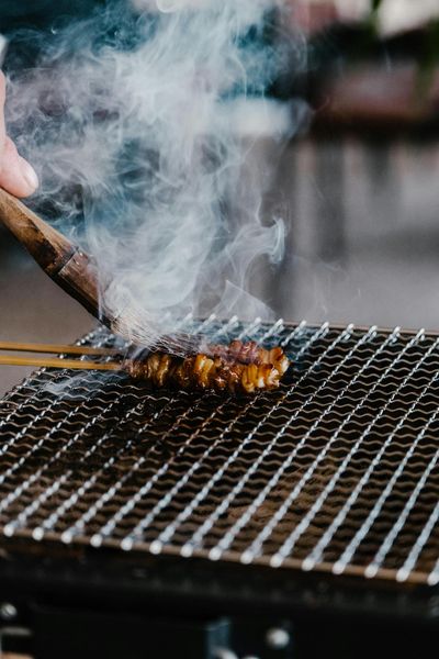 Close-up of juicy skewered meat grilling with smoke rising on a barbecue.