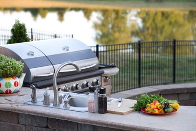 bbq area - Preparing a healthy summer meal in an outdoor kitchen with gas barbecue and sink on a brick patio overlooking a tr