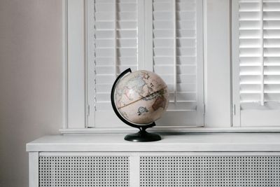 Elegant globe on a minimalist white desk against shuttered windows in modern interior design.