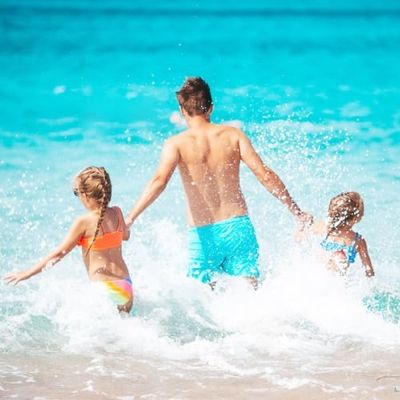 Happy father and little daughters on beach vacation play in shallow water