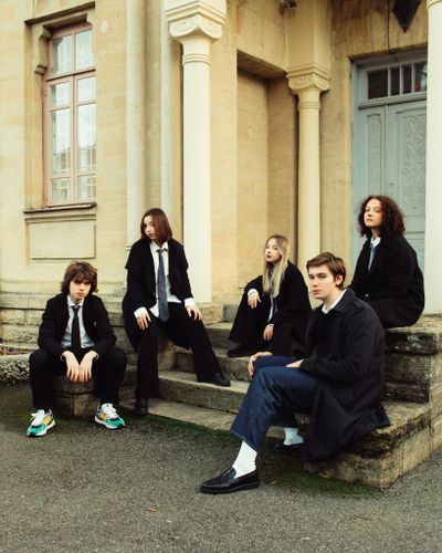 Five teenagers in school uniforms seated on steps of a classical building, Russia.
