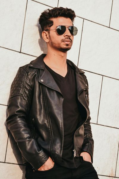 Man in Black Leather Jacket Leaning on White Concrete Wall