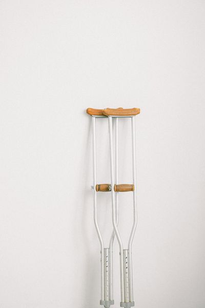 Minimalist image of crutches leaning on a white wall indoors.