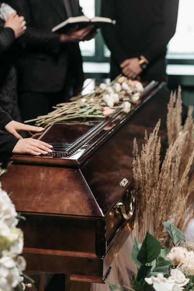 Mourners at a funeral with floral arrangements on a polished wooden coffin.