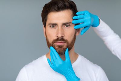 Photo plastic surgery and aesthetic cosmetology concept cosmetician hands in protective medical gloves touching male face