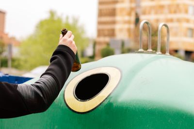 A man's hand recycling a glass bottle into a skip bin container. Recycling and caring for the environment concept