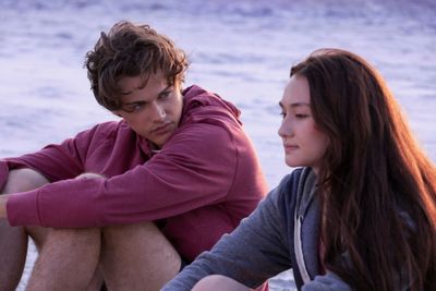 Christopher Briney as Conrad and Lola Tung as Belly sitting on the beach in The Summer I Turned Pretty