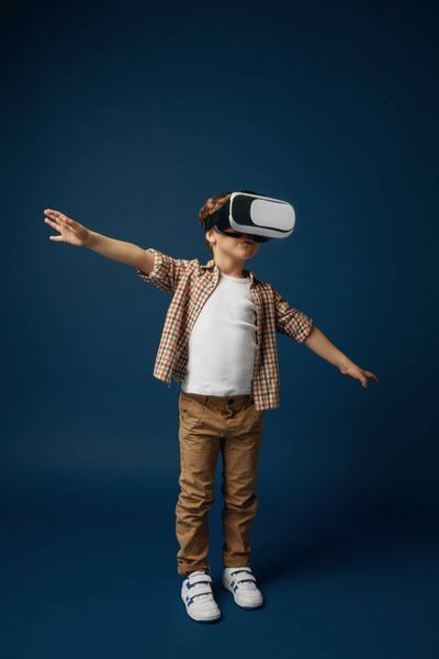 Weightless in the sky. little boy or child in jeans and shirt with virtual reality headset glasses isolated on blue studio ba