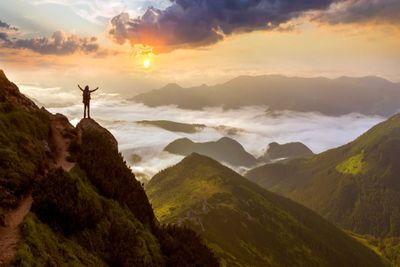 Photo wide mountain panorama. small silhouette of tourist with backpack on rocky mountain slope with raised hands over valley