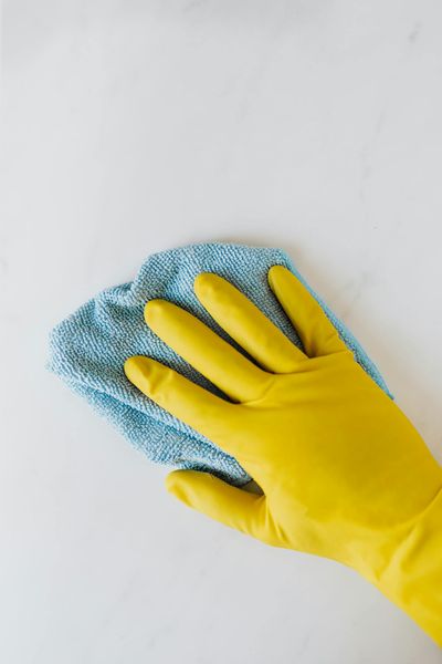 Yellow gloved hand wiping surface with blue cloth, concept of cleaning and hygiene.