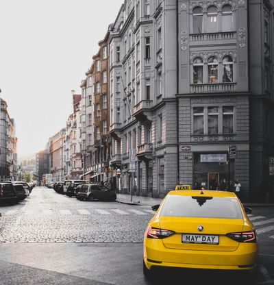 Yellow taxi in a classic Prague street with historical architecture under daylight.