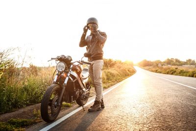 Young handsome man posing near his motorbike at countryside road.
