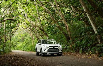 2026 Toyota Grand Highlander Hybrid MAX Platinum driving on a wooded road exterior view