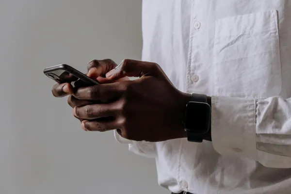 A close-up shot of a person wearing a smartwatch and typing on a smartphone indoors.