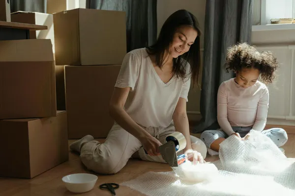 A mother and daughter packing boxes while preparing for a move in a sunlit room.