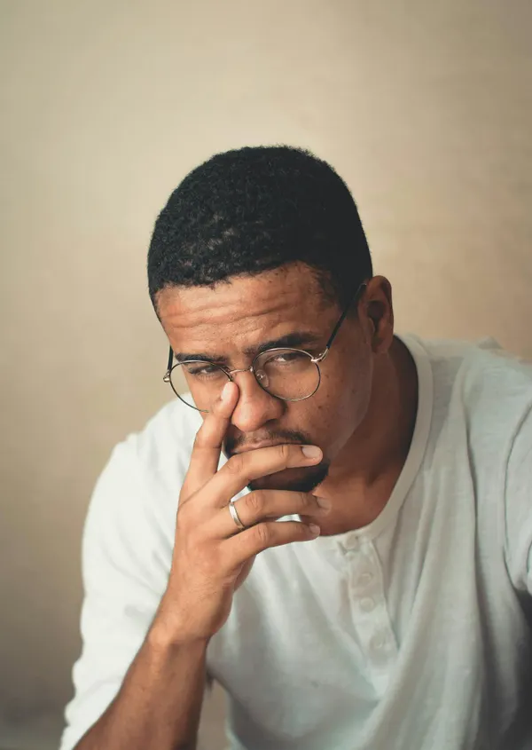 A pensive man with glasses and facial hair, posing indoors, looking contemplative.