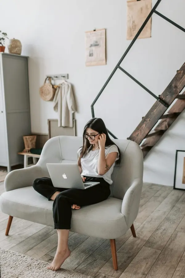 A woman sits comfortably on a sofa using a laptop in a modern living room.