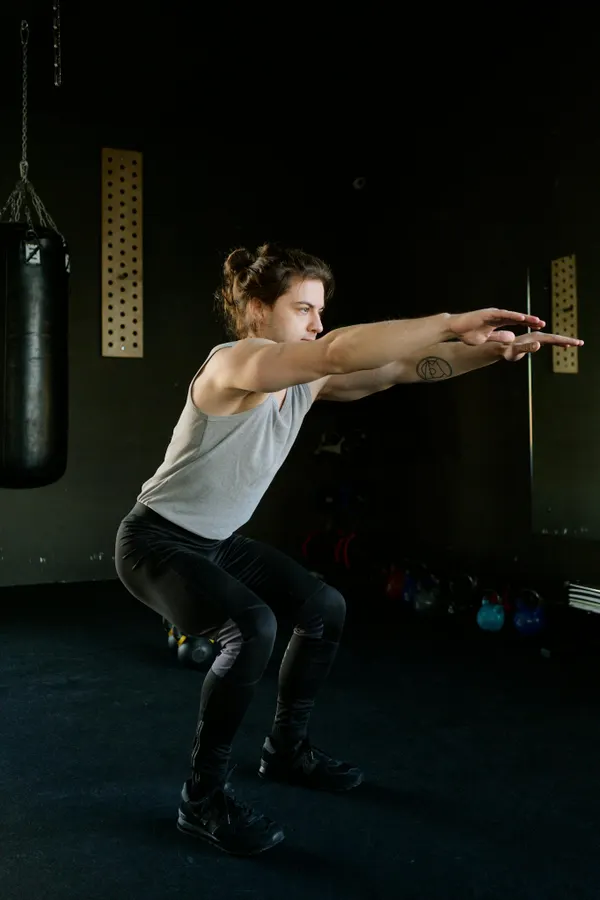A young man performing squats in an indoor gym setting focusing on fitness and strength training.