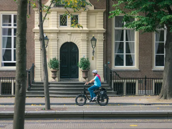 Adult cyclist wearing helmet rides through city street past historic building.
