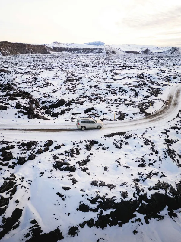 Aerial view of an SUV navigating a snowy Icelandic landscape, capturing winter's serene isolation.