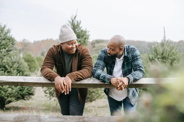 African American teen man having conversation with dad leaning on fence standing against green trees and looking at each othe