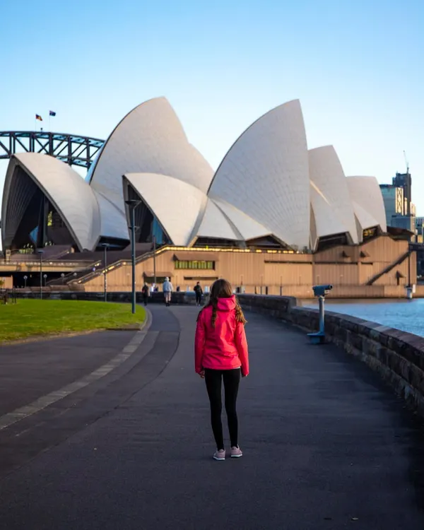 Photo beautiful girl walks by famous sydney opera house at sunrise, sunrise over sydney opera house, aus
