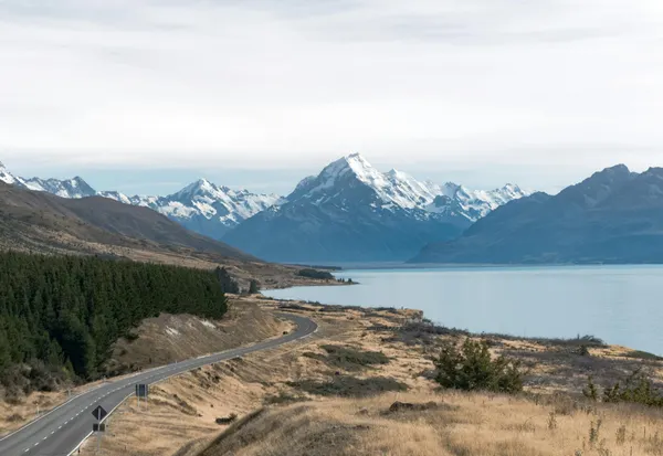 Breathtaking view of Mount Cook with a winding road, lake, and snow-capped peaks in New Zealand.