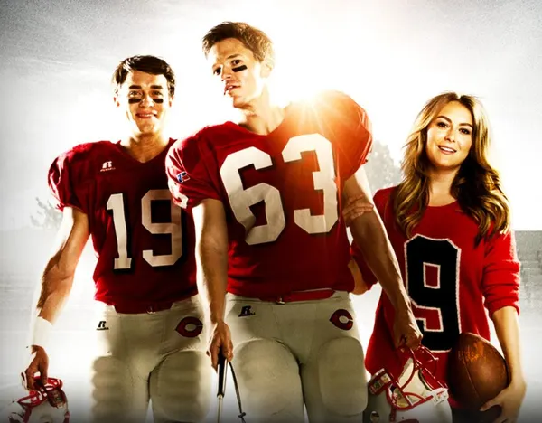 Promotional image from 23 Blast featuring three main characters standing together on a football field. Two young men wear red