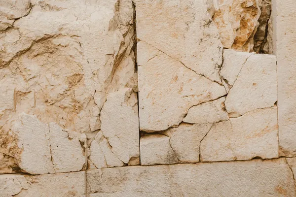 Close-up of a textured beige stone wall with cracks and rough surface.
