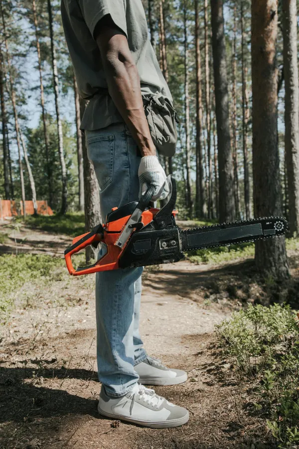 Close-up of an arborist holding a chainsaw in a wooded area.
